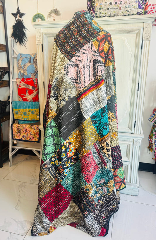 A handcrafted silk patchwork quilt with a floral pattern, displayed on a hanger, with various colors including black, red, blue, and green visible.