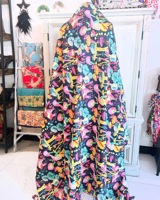 A handblock printed quilt with a black background featuring a vibrant mushroom pattern on one side, displayed in a room setting.