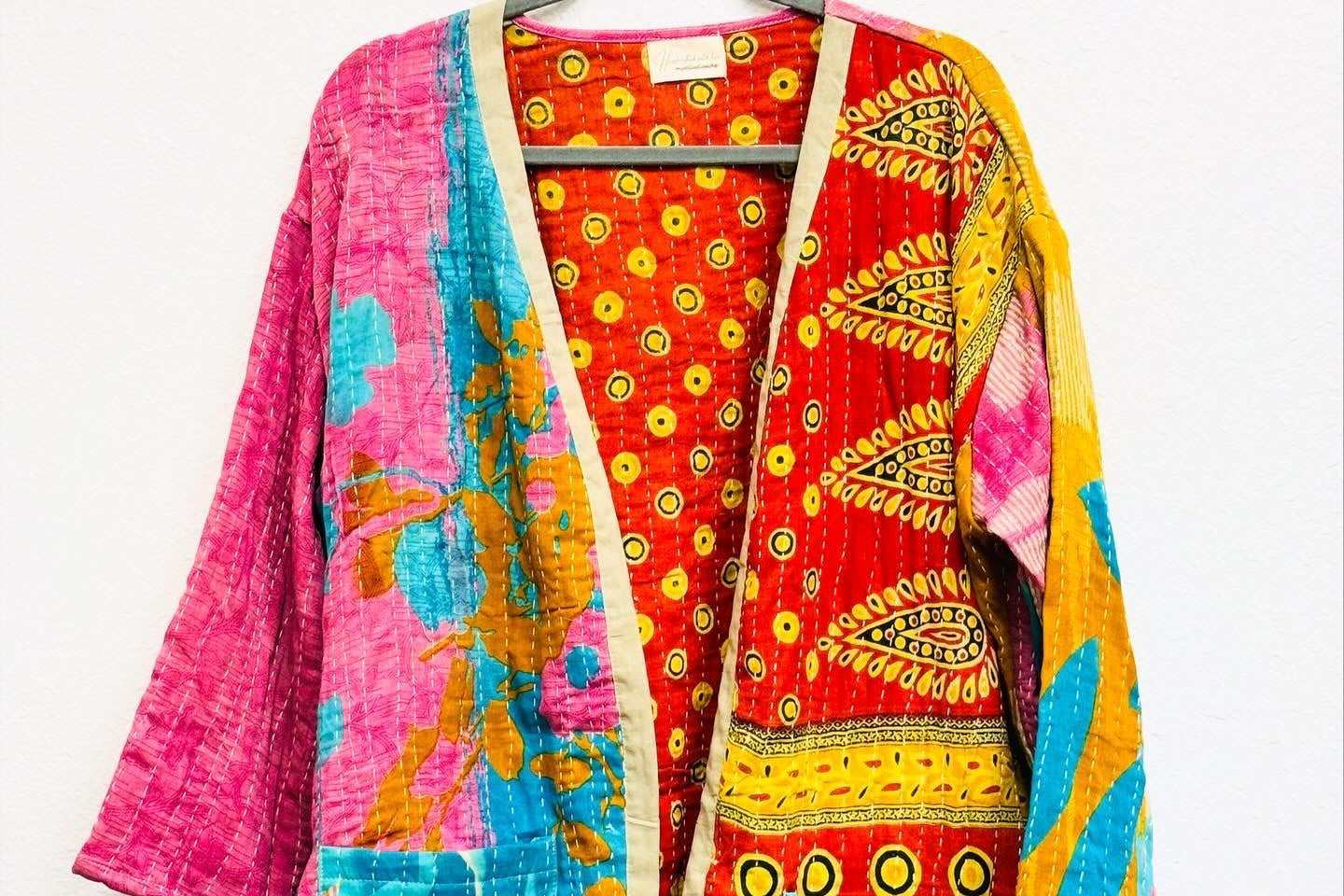 A multicolored floral kimono with pink and blue predominantly, displayed on a hanger.