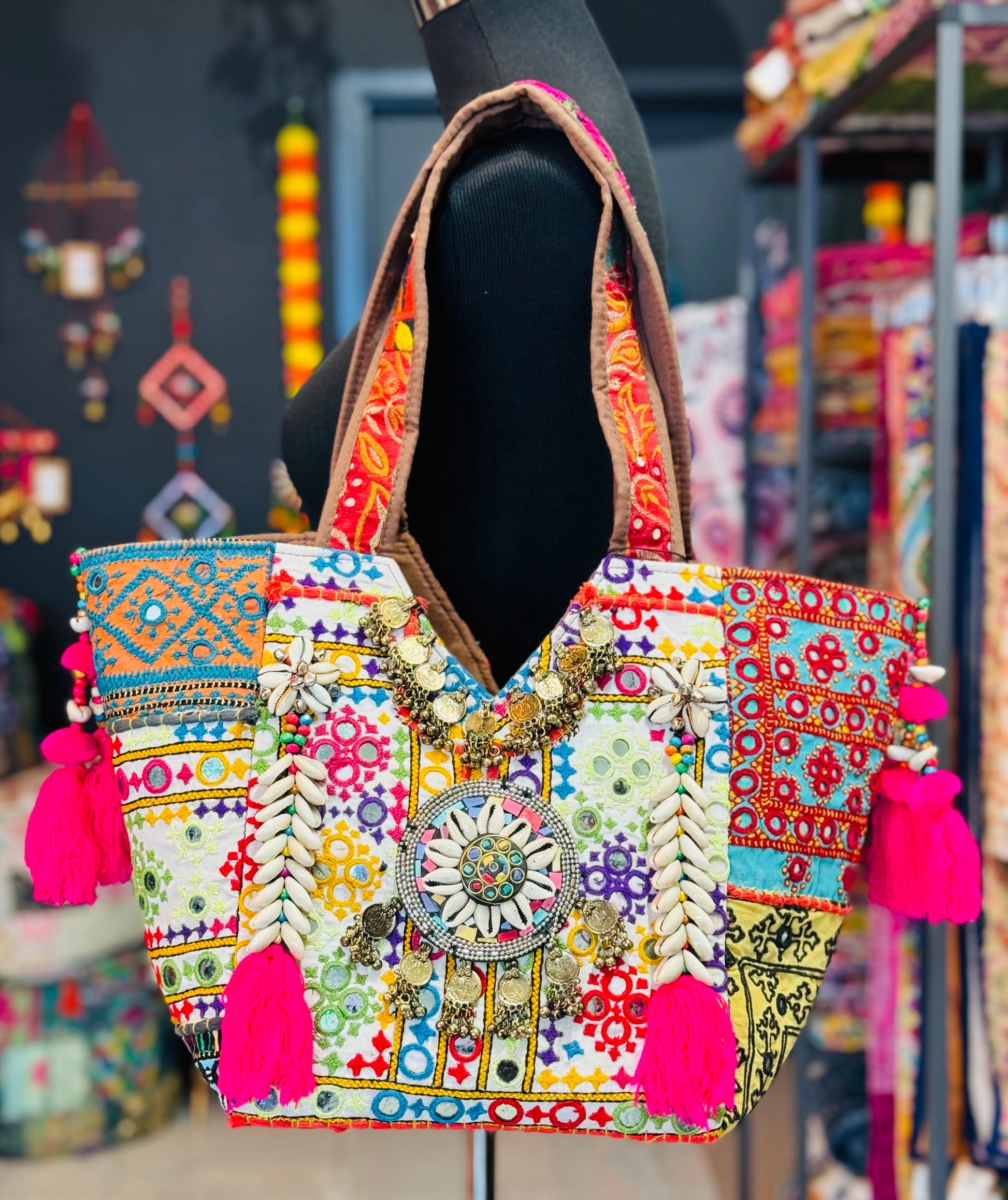 Vibrant white banjara tote bag with multi color embroidered patches, mirror work, cowrie shells, hot pink tassels.