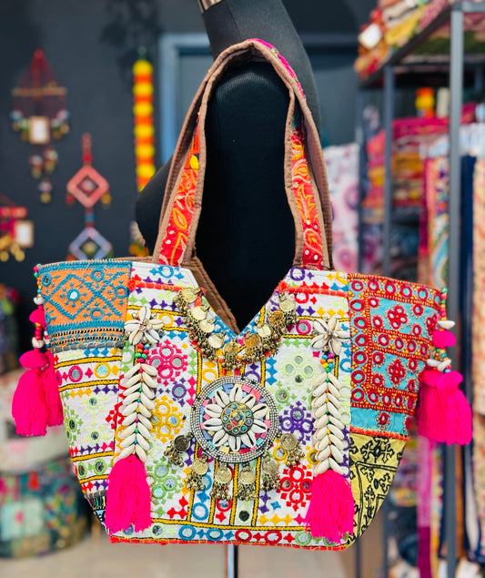 Vibrant white banjara tote bag with multi color embroidered patches, mirror work, cowrie shells, hot pink tassels.