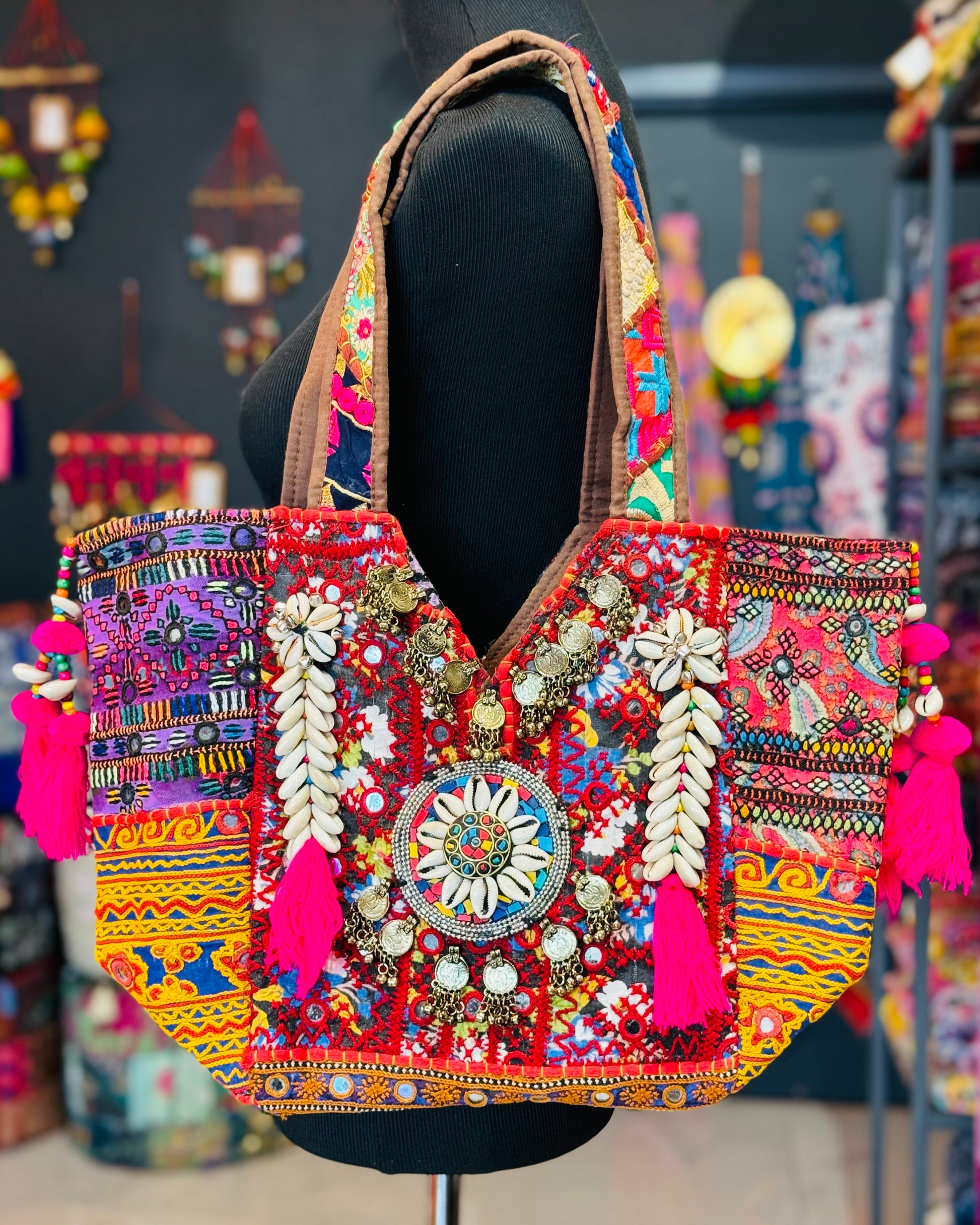 Multicolor banjara tote bag with multi color embroidered patches, mirror work, cowrie shells, hot pink tassels. Purple patch on one side and salmon patch on the other side.