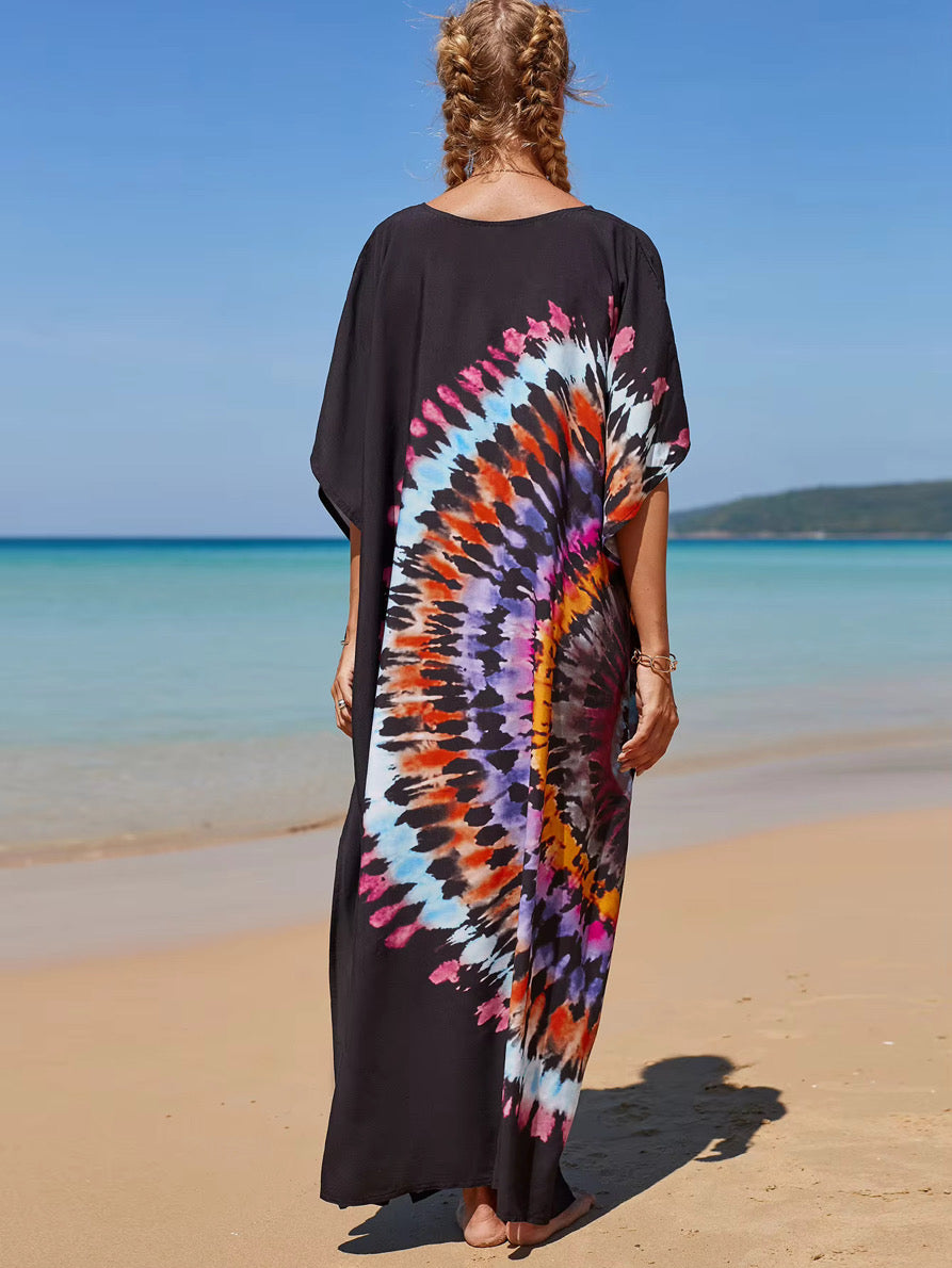 Person wearing a black kaftan dress with a colorful tie-dye pattern on a beach.