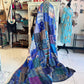 Colorful patchwork quilt draped over a mannequin in a store setting with various items on shelves.