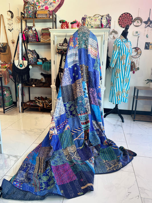 Colorful patchwork quilt draped over a mannequin in a store setting with various items on shelves.