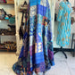 Colorful silk and cotton handmade patchwork kantha quilt draped over a mannequin in a store setting with various items in the background.