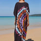 Person wearing a black kaftan dress with a colorful tie-dye pattern on a beach.